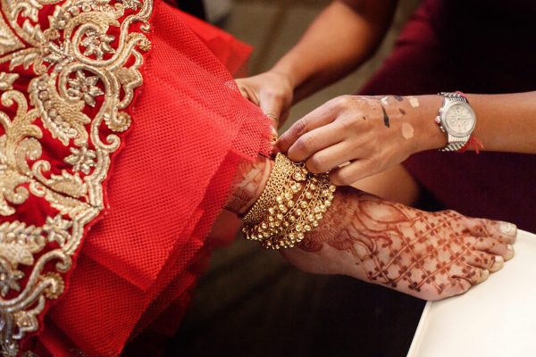 Woman puts golden bracelet with bells on bride's leg painted with mehndi